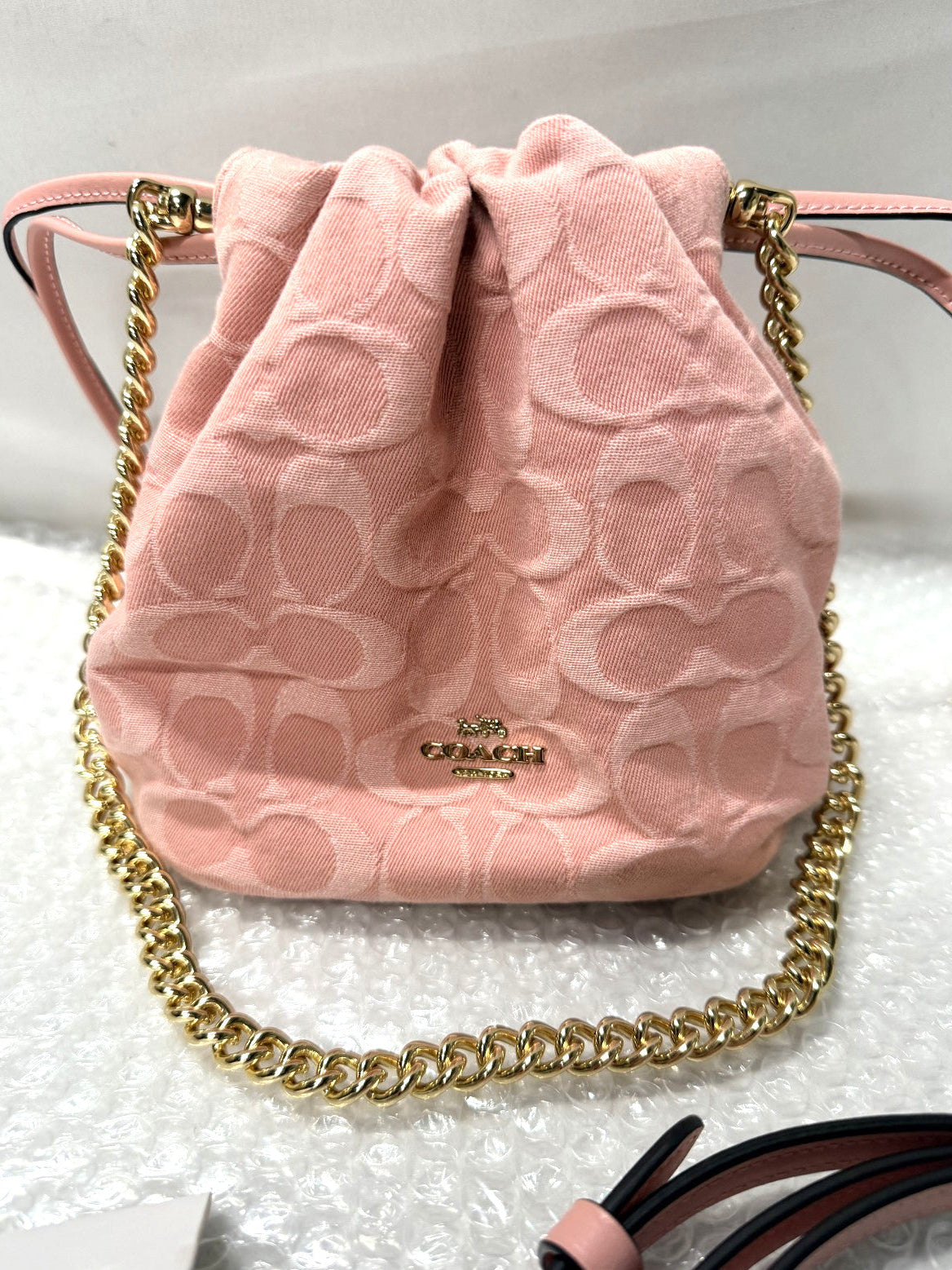 Pink drawstring bag with gold chain on a white background